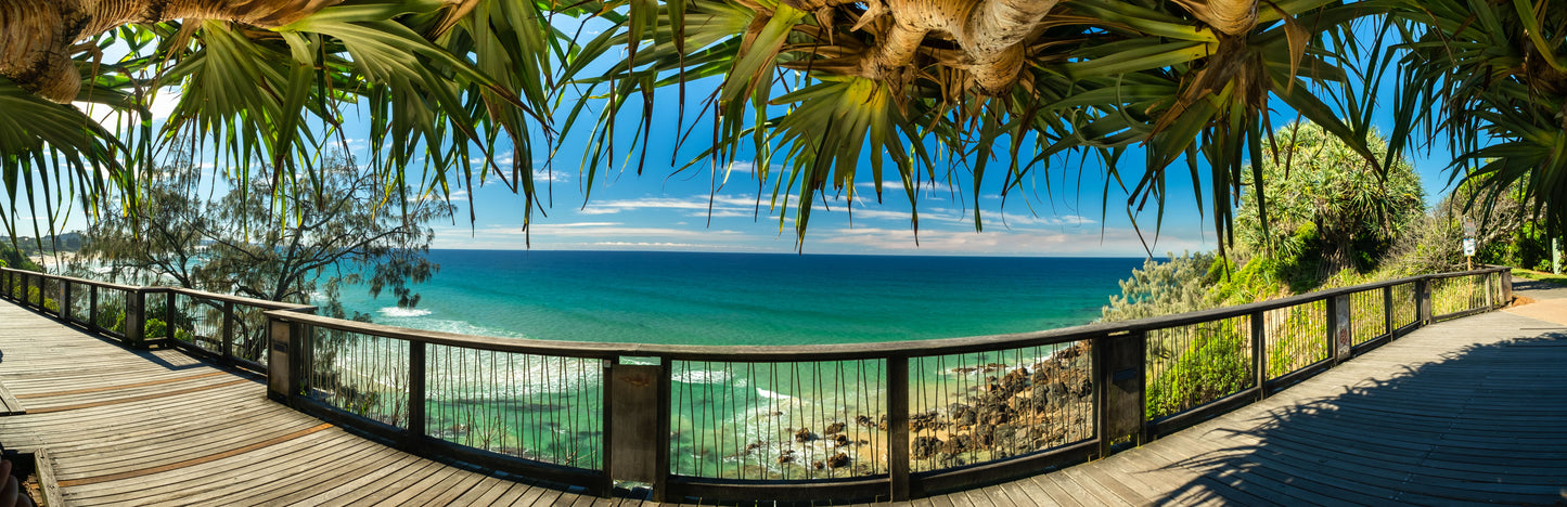 Panoramic view of a coastal landscape with a wooden deck, ocean, and blue sky.